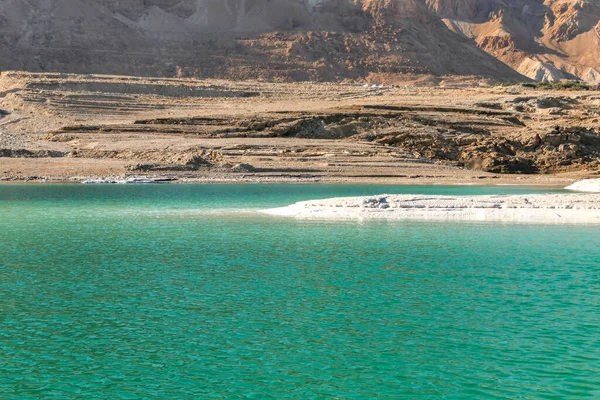 Tuz oluşumlarıyla kaplı kıyıdan Ölü Deniz 'in sularının ötesindeki dağların görüntüsü.