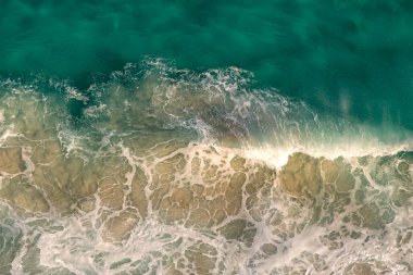 Okyanus dalgalarının kıyı kayalarına çarpmasından kaynaklanan beyaz köpük desenlerinin üst görüntüsü. Güney Afrika