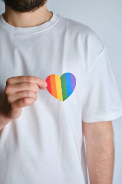 Rainbow heart from paper in man hands in white t-shirt. LGBT flag. LGBTQIA Pride Month in June. Lesbian Gay Bisexual Transgender. Gender equality. Human rights and tolerance. Rainbow flag