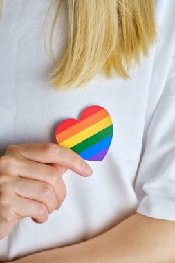 Rainbow heart from paper in woman hands in white t-shirt. LGBT flag. LGBTQIA Pride Month in June. Lesbian Gay Bisexual Transgender. Gender equality. Human rights and tolerance. Rainbow flag