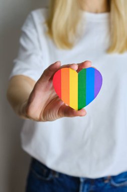 Rainbow heart from paper in woman hands in white t-shirt. LGBT flag. LGBTQIA Pride Month in June. Lesbian Gay Bisexual Transgender. Gender equality. Human rights and tolerance. Rainbow flag