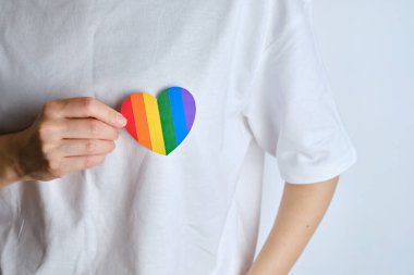 Rainbow heart from paper in woman hands in white t-shirt. LGBT flag. LGBTQIA Pride Month in June. Lesbian Gay Bisexual Transgender. Gender equality. Human rights and tolerance. Rainbow flag