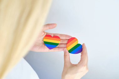 Rainbow heart from paper in woman hands in white t-shirt. LGBT flag. LGBTQIA Pride Month in June. Lesbian Gay Bisexual Transgender. Gender equality. Human rights and tolerance. Rainbow flag