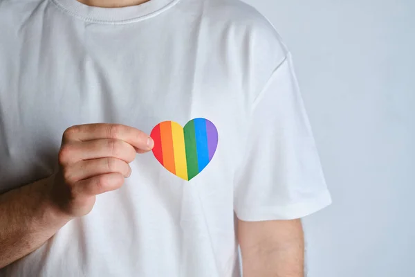 Rainbow heart from paper in man hands in white t-shirt. LGBT flag. LGBTQIA Pride Month in June. Lesbian Gay Bisexual Transgender. Gender equality. Human rights and tolerance. Rainbow flag