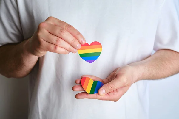 Rainbow heart from paper in man hands in white t-shirt. LGBT flag. LGBTQIA Pride Month in June. Lesbian Gay Bisexual Transgender. Gender equality. Human rights and tolerance. Rainbow flag