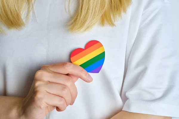 Rainbow heart from paper in woman hands in white t-shirt. LGBT flag. LGBTQIA Pride Month in June. Lesbian Gay Bisexual Transgender. Gender equality. Human rights and tolerance. Rainbow flag