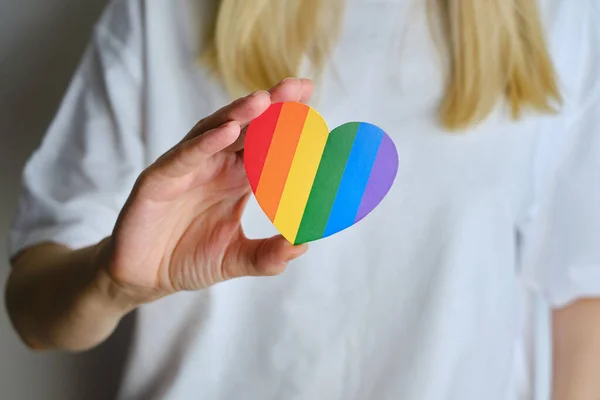 Rainbow heart from paper in woman hands in white t-shirt. LGBT flag. LGBTQIA Pride Month in June. Lesbian Gay Bisexual Transgender. Gender equality. Human rights and tolerance. Rainbow flag