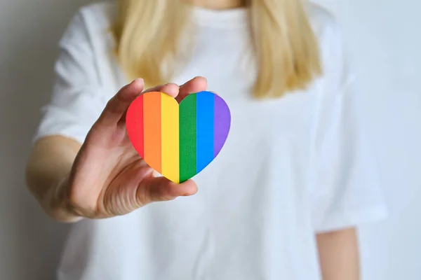 Rainbow heart from paper in woman hands in white t-shirt. LGBT flag. LGBTQIA Pride Month in June. Lesbian Gay Bisexual Transgender. Gender equality. Human rights and tolerance. Rainbow flag