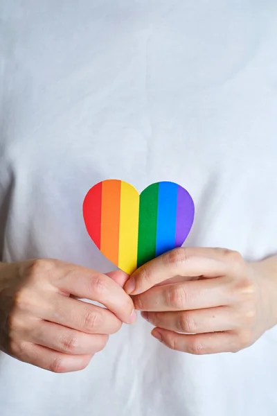 Rainbow heart from paper in woman hands in white t-shirt. LGBT flag. LGBTQIA Pride Month in June. Lesbian Gay Bisexual Transgender. Gender equality. Human rights and tolerance. Rainbow flag