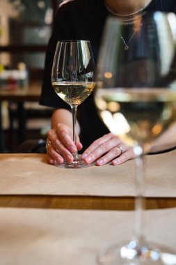 A glass of white wine in the hands of a girl relaxing in a restaurant. Tasting of alcoholic beverages. Summer rest. Romantic evening aperitif. Close-up of a glass of wine. Enjoy the moment