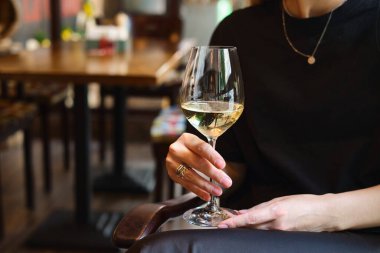 A glass of white wine in the hands of a girl relaxing in a restaurant. Tasting of alcoholic beverages. Summer rest. Romantic evening aperitif. Close-up of a glass of wine. Enjoy the moment