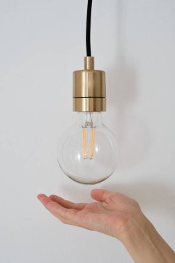 The girl's hand points to the lamp. The concept of energy saving and environmentally friendly consumption. Close-up lamp on a light background. Concept idea with innovation and inspiration
