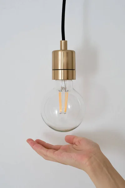 The girl\'s hand points to the lamp. The concept of energy saving and environmentally friendly consumption. Close-up lamp on a light background. Concept idea with innovation and inspiration