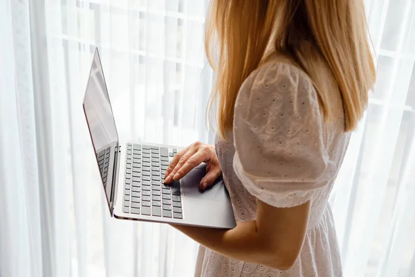 The girl works for a laptop near the window. Remote work from home or hotel. Business woman at work in the office. Business background. Home office