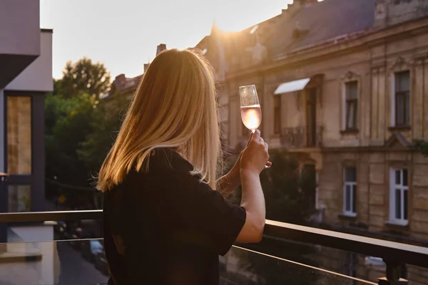 Girl with a glass of rose wine on the balcony. Drinks rose wine and enjoy the moment. A celebration holiday alone. Relaxed lifestyle. Happy woman rest after work. Beautiful European courtyard