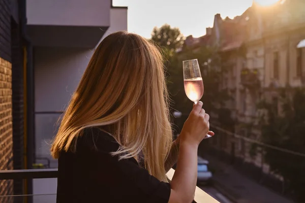 Girl with a glass of rose wine on the balcony. Drinks rose wine and enjoy the moment. A celebration holiday alone. Relaxed lifestyle. Happy woman rest after work. Beautiful European courtyard