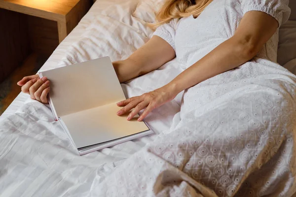 A girl reads a book in bed in the morning or before bedtime. Leisure and recreation concept. Close-up book in the hands of a girl. Place for your text
