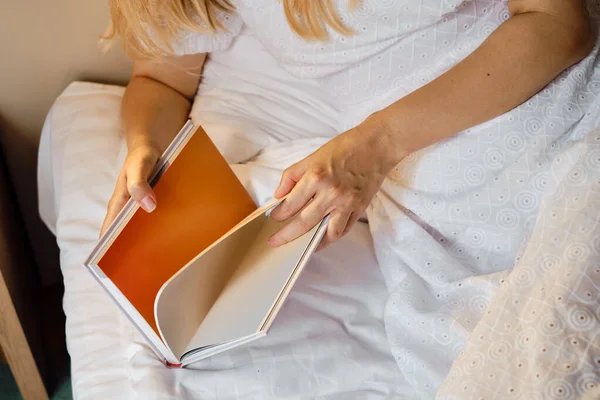 A girl reads a book in bed in the morning or before bedtime. Leisure and recreation concept. Close-up book in the hands of a girl. Place for your text