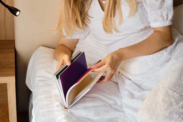 A girl reads a book in bed in the morning or before bedtime. Leisure and recreation concept. Close-up book in the hands of a girl. Place for your text