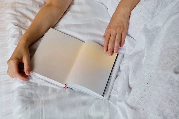 A girl reads a book in bed in the morning or before bedtime. Leisure and recreation concept. Close-up book in the hands of a girl. Place for your text