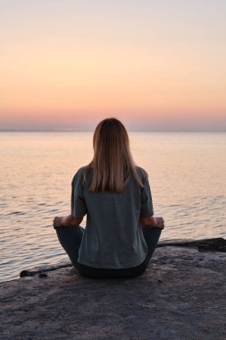 A woman is engaged in meditation near the sea on the pier. Sunrise Meditation. Healthy lifestyle, active rest. Morning yoga near the sea. Tourism, travel and yoga concept