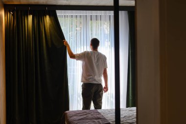 The man stretches after getting out of bed and looking out the window. Morning rituals for a vigorous workday. Health and relaxation concept