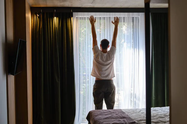 The man stretches after getting out of bed and looking out the window. Morning rituals for a vigorous workday. Health and relaxation concept