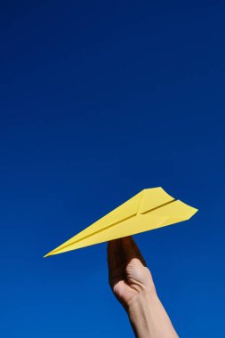 Paper yellow plane in the hands against the blue sky. Taking flight! Travel concept