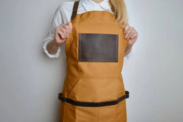 A woman in a kitchen apron. Chef work in the cuisine. Cook in uniform, protection apparel. Job in food service. Professional culinary. Camel fabric apron, casual clothing. Handsome baker posing