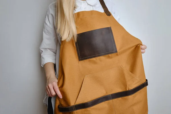 A woman in a kitchen apron. Chef work in the cuisine. Cook in uniform, protection apparel. Job in food service. Professional culinary. Camel fabric apron, casual clothing. Handsome baker posing