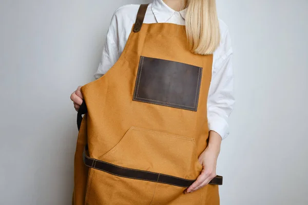 A woman in a kitchen apron. Chef work in the cuisine. Cook in uniform, protection apparel. Job in food service. Professional culinary. Camel fabric apron, casual clothing. Handsome baker posing