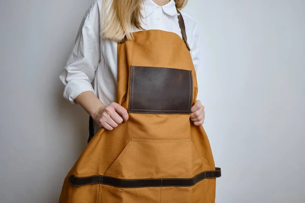 A woman in a kitchen apron. Chef work in the cuisine. Cook in uniform, protection apparel. Job in food service. Professional culinary. Camel fabric apron, casual clothing. Handsome baker posing