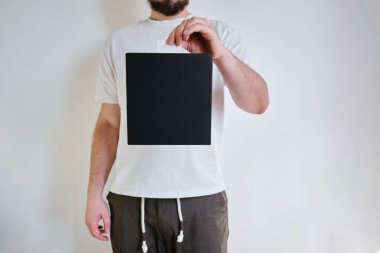 Man holds a black paper box in his hand. Young man with new package. Postal services, delivery. Kraft paper. Gift box, gift. Box close-up. Empty packaging, empty space. Cardboard case