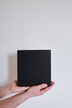Man holds a black paper box in his hand. Young man with new package. Postal services, delivery. Kraft paper. Gift box, gift. Box close-up. Empty packaging, empty space. Cardboard case