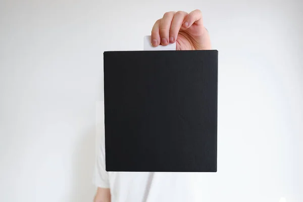 Man holds a black paper box in his hand. Young man with new package. Postal services, delivery. Kraft paper. Gift box, gift. Box close-up. Empty packaging, empty space. Cardboard case