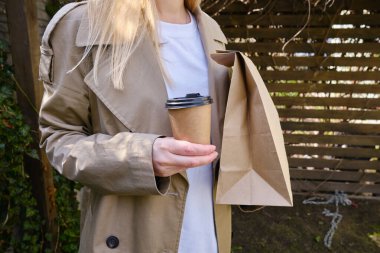 A paper glass and a craft bag in the hands of a girl. A glass for coffee and hot drinks to go. Food delivery service. Paper bag close up. Blank space mockup for design, lettering or advertising