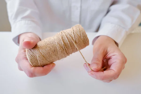 A skein of jute twine in the hands on a white background. Natural rope for packaging and decoration. Coarse linen thread. Hemp twine