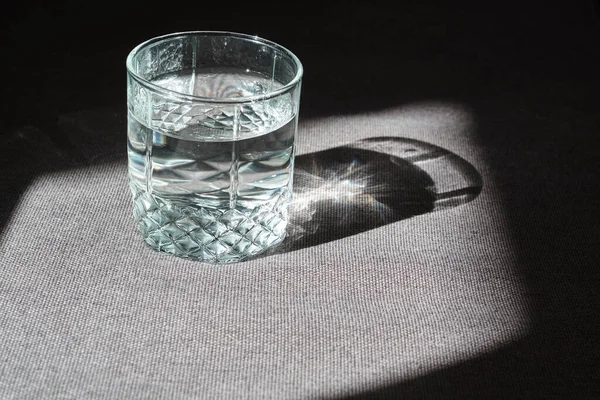 Transparent glass with drinking clean water in the sun on a dark background. The concept of a healthy lifestyle, skin care. A glass of water close-up. Healthy food. Body water balance for health