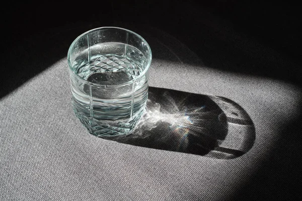 Transparent glass with drinking clean water in the sun on a dark background. The concept of a healthy lifestyle, skin care. A glass of water close-up. Healthy food. Body water balance for health