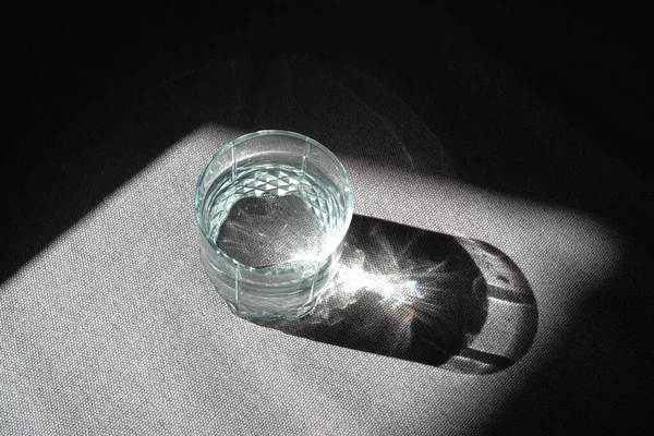 Transparent glass with drinking clean water in the sun on a dark background. The concept of a healthy lifestyle, skin care. A glass of water close-up. Healthy food. Body water balance for health