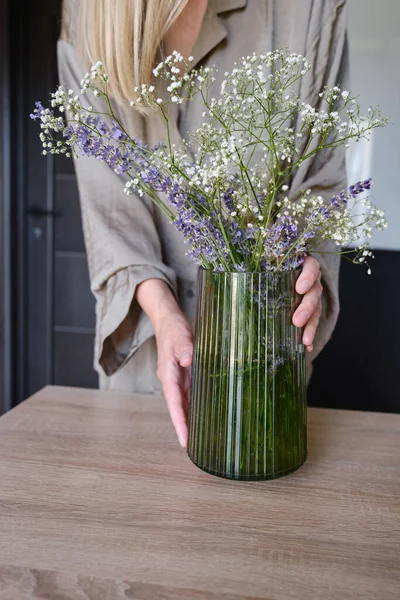 Girl florist collects a beautiful bouquet. Bouquet in a vase on the table for home decoration. Beautiful green vase with lavender flowers