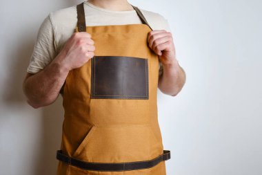 A man in a kitchen apron. Chef work in the cuisine. Cook in uniform, protection apparel. Job in food service. Professional culinary. Camel fabric apron, casual stylish clothing. Handsome baker posing