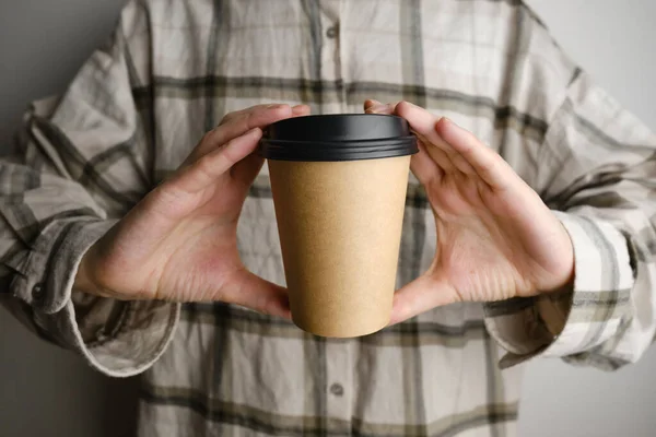 Disposable paper cup close-up. Eco material. Glass for hot drinks. Empty space for text, mockup. Craft paper cup with coffee in a female hand. Coffee to go concept