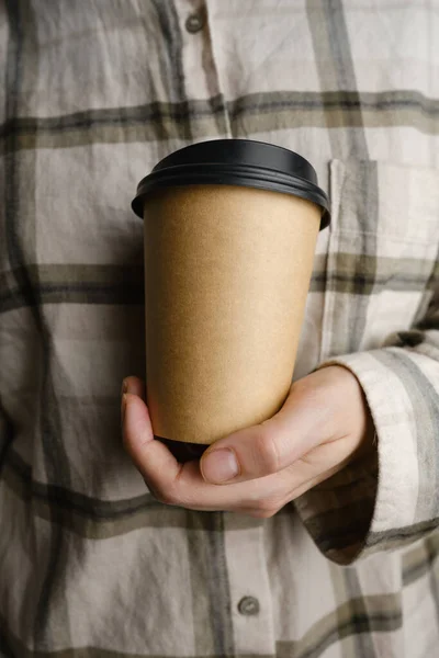 Disposable paper cup close-up. Eco material. Glass for hot drinks. Empty space for text, mockup. Craft paper cup with coffee in a female hand. Coffee to go concept