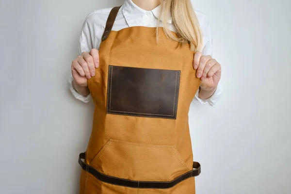 A woman in a kitchen apron. Chef work in the cuisine. Cook in uniform, protection apparel. Job in food service. Professional culinary. Camel fabric apron, casual clothing. Handsome baker posing