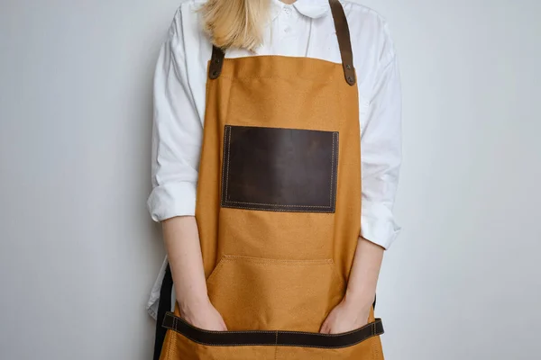 A woman in a kitchen apron. Chef work in the cuisine. Cook in uniform, protection apparel. Job in food service. Professional culinary. Camel fabric apron, casual clothing. Handsome baker posing