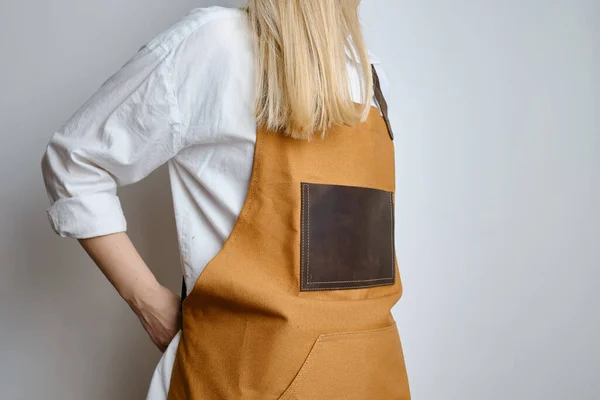 A woman in a kitchen apron. Chef work in the cuisine. Cook in uniform, protection apparel. Job in food service. Professional culinary. Camel fabric apron, casual clothing. Handsome baker posing