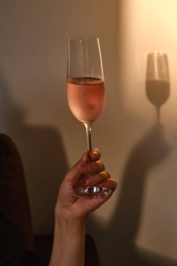 Evde güneşin batışında bir kızın elinde bir bardak gül şarabı vardı. Alkollü içecekler tatmak. Kutlayın ve anın tadını çıkarın. Romantik akşam aperatifi. Yakın plan şarap kadehi.