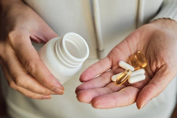 Woman pours pills or vitamins from a jar onto her hand. Taking vitamins or medications. The concept of health care, medicine, pharmacies, disease prevention. A jar with pills or vitamins in the hands