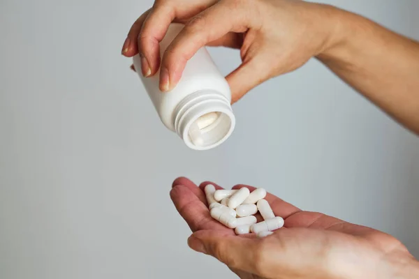 Woman pours pills or vitamins from a jar onto her hand. Taking vitamins or medications. The concept of health care, medicine, pharmacies, disease prevention. A jar with pills or vitamins in the hands